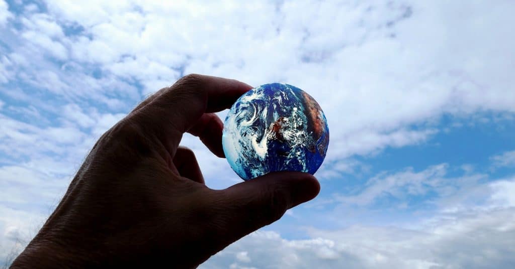 Hand holding the earth with a cloudy sky above