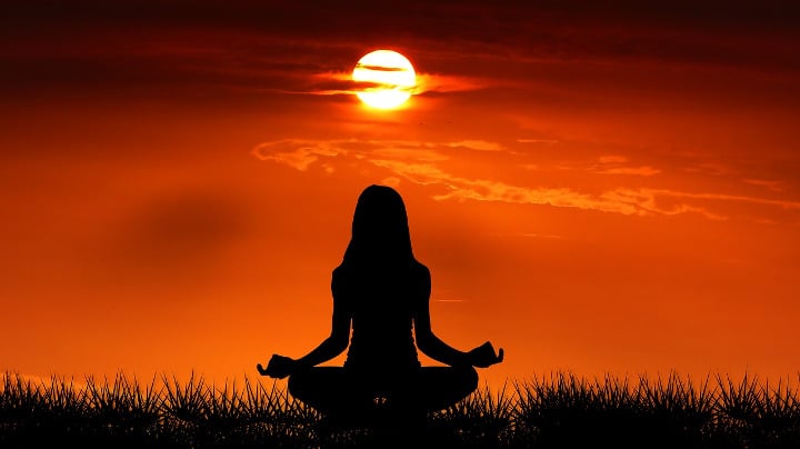 outline of a woman meditating under a sunset